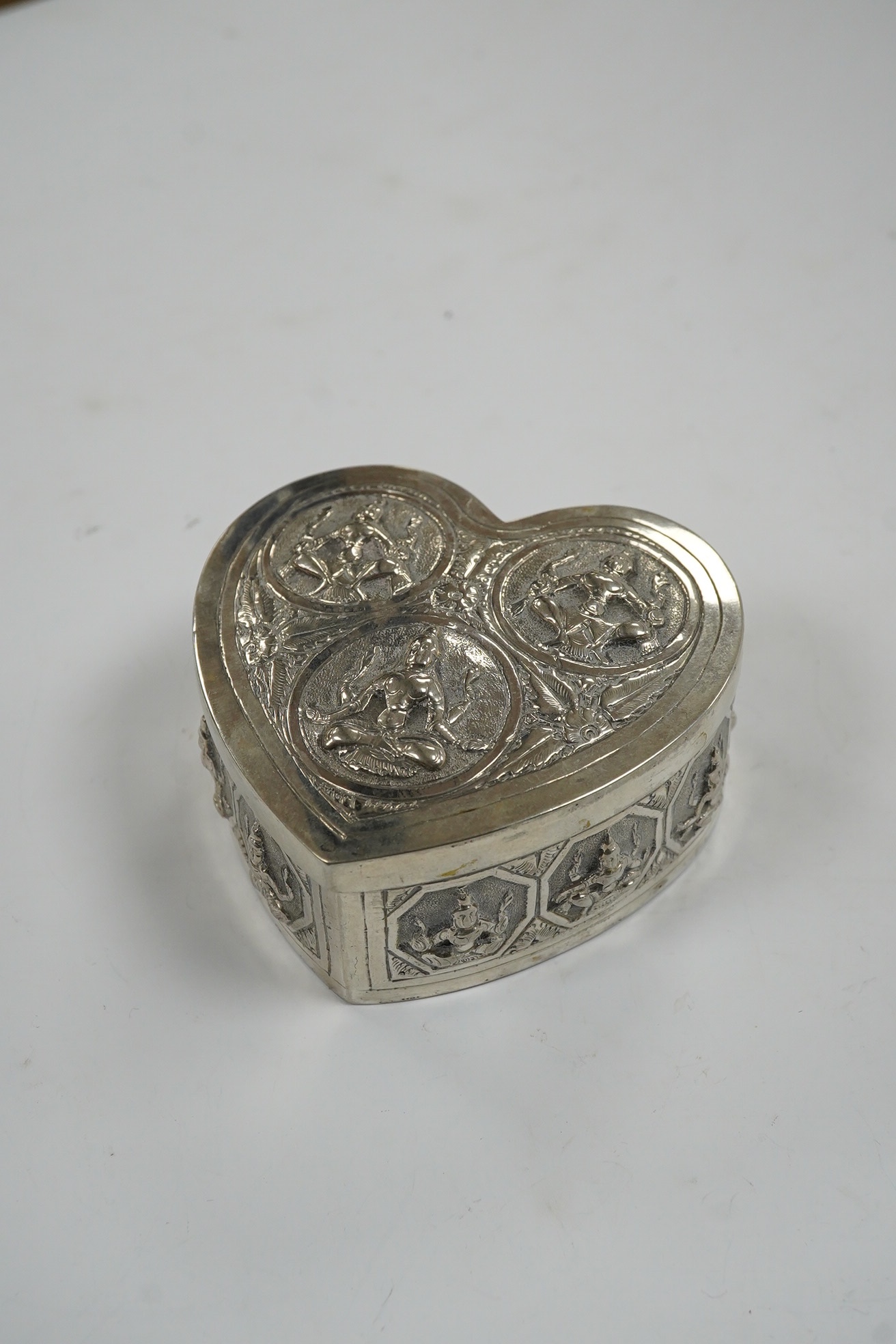 An Indian embossed white metal heart shaped trinket box and cover, width 85mm, 120 grams. Condition - fair